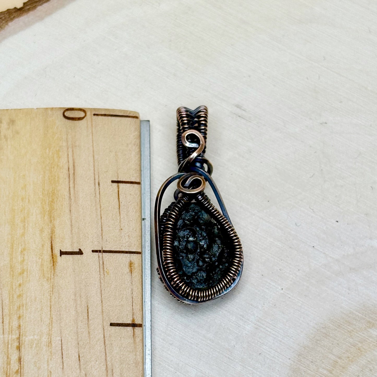 Decorative pendant with a natural stone center on a wooden surface with a ruler for scale.