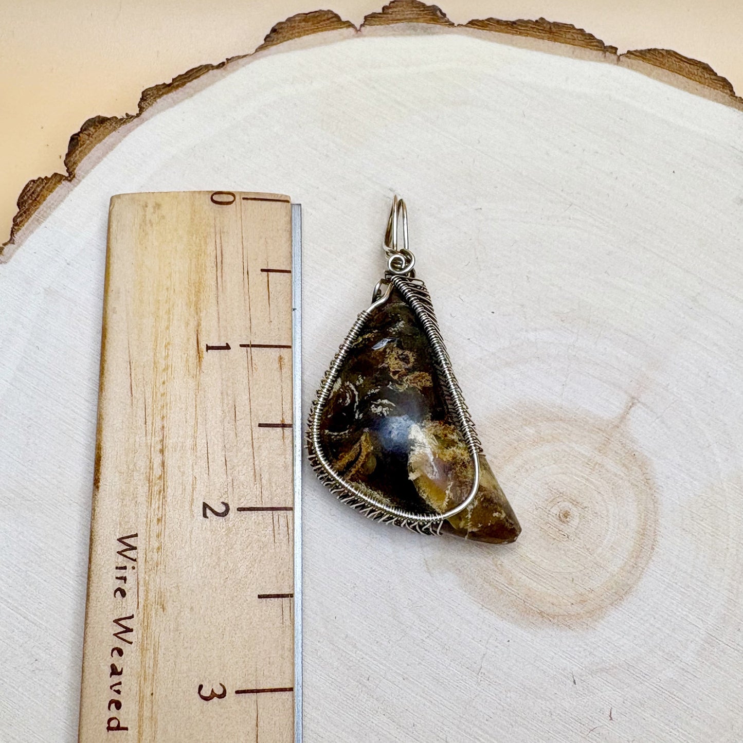 Pendant with a stone-like design on a wooden surface next to a ruler.