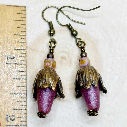 Pair of earrings with purple and gold bronze beads on a wooden surface with a ruler.