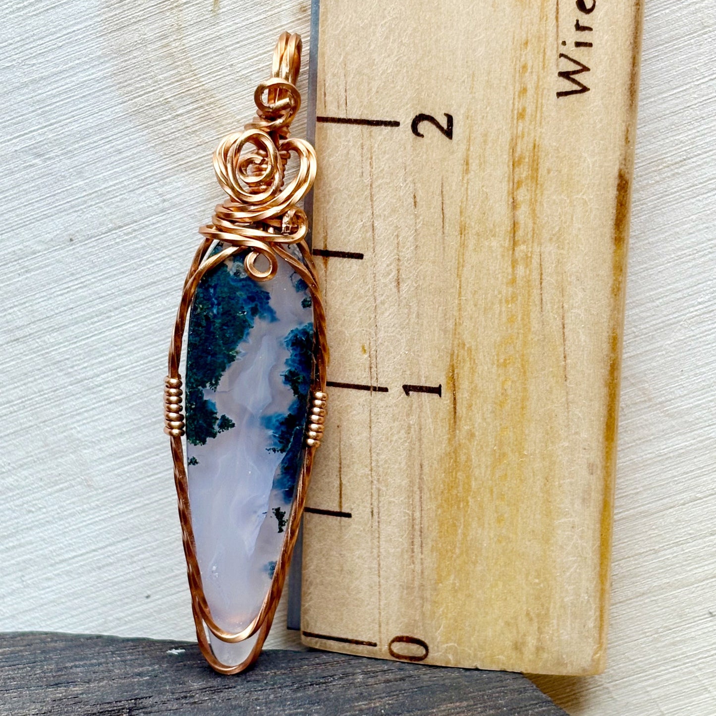 Copper moss agate pendant on a wooden background with a ruler