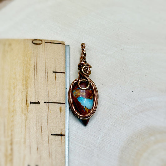 Pendant with a opal stone on a wooden surface with a ruler for scale.