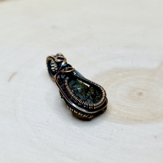 Moldavite Jewelry pendant with a textured surface on a light wooden background