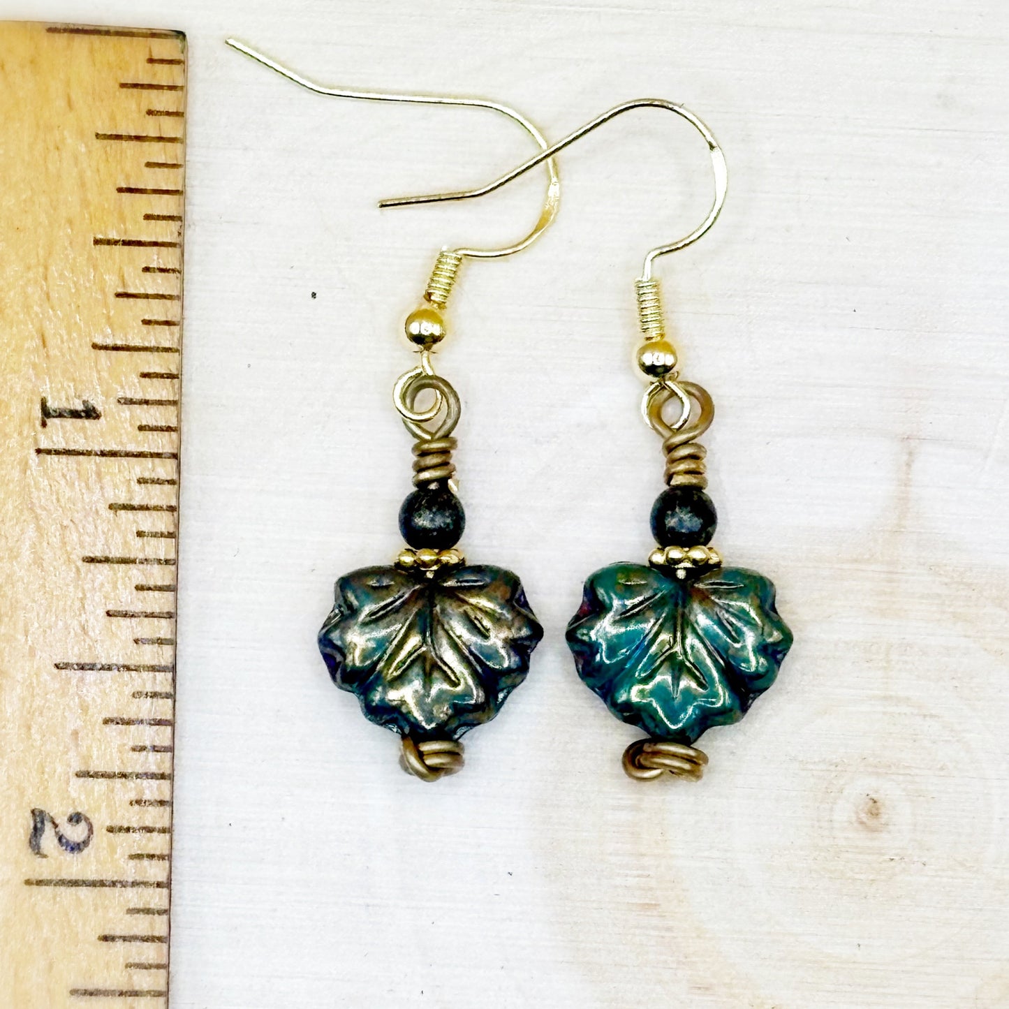 Pair of leaf-shaped earrings with gold accents on a white background with a ruler for scale.