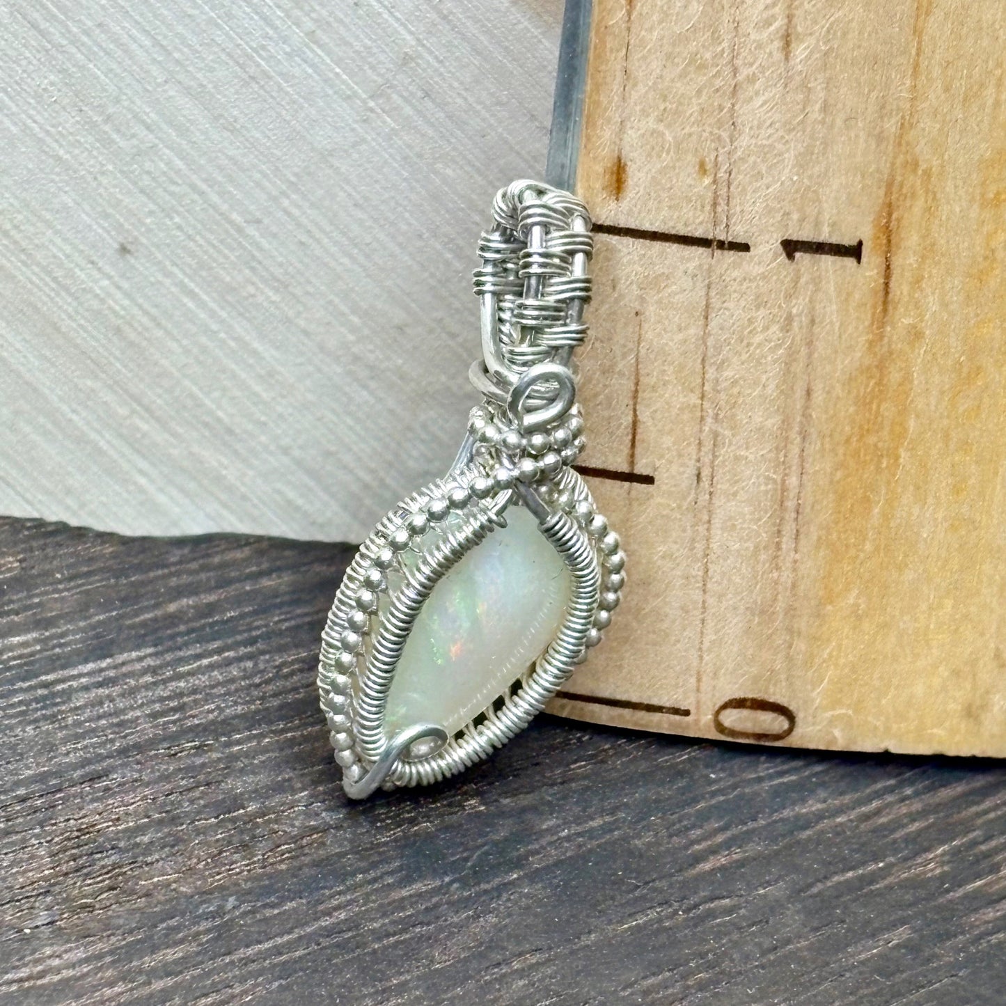 Sterling silver dainty opal pendant on a wooden background with a ruler
