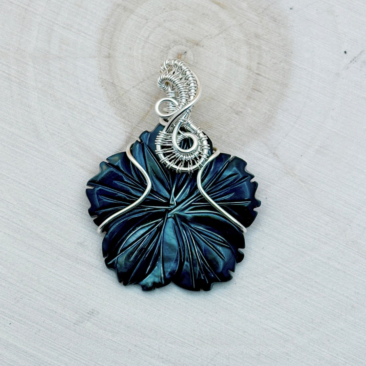 Blue flower shaped pendant with silver wire wrapping on a light background