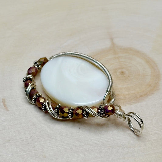 Pendant with a white shell and beaded wirework on a wooden surface