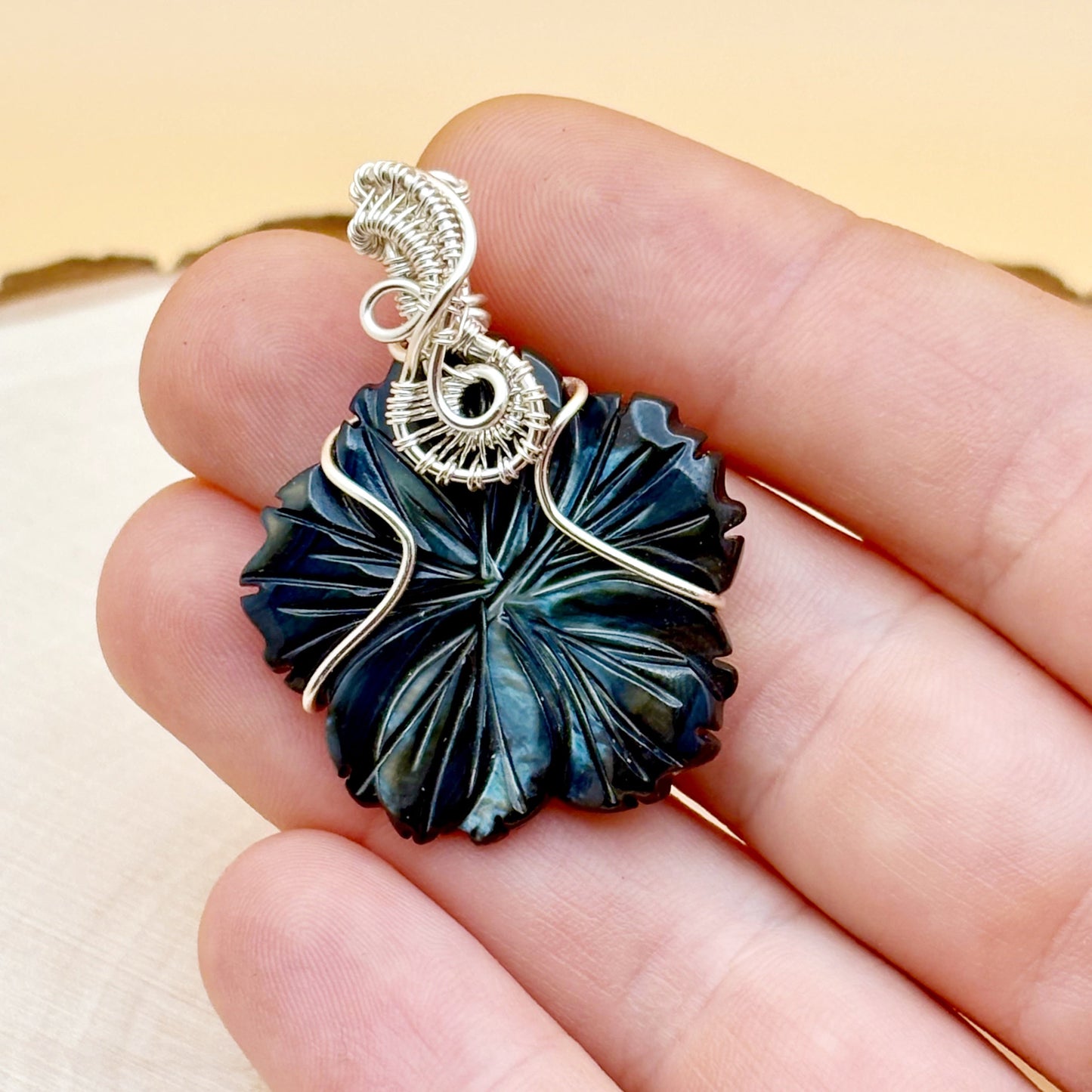 Decorative pendant held between fingers with a neutral background