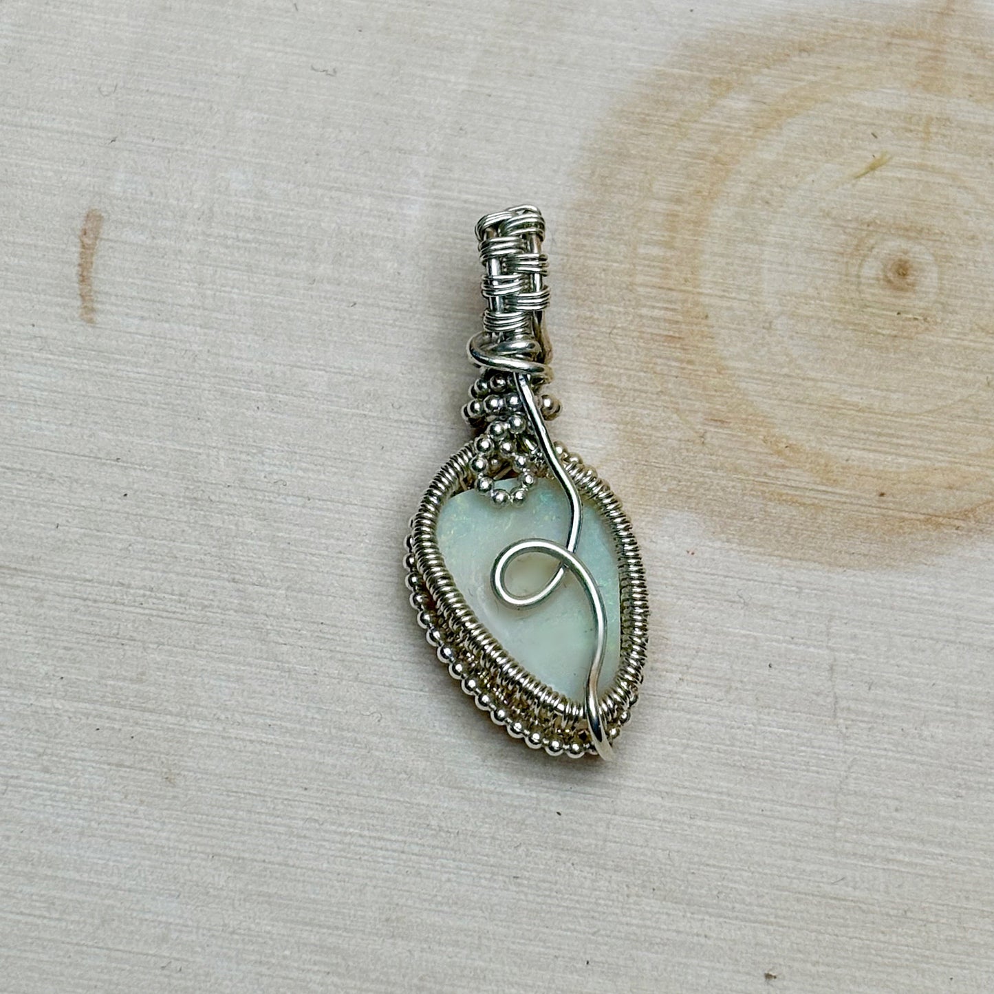 Silver wire-wrapped pendant with an opal center on a wooden surface