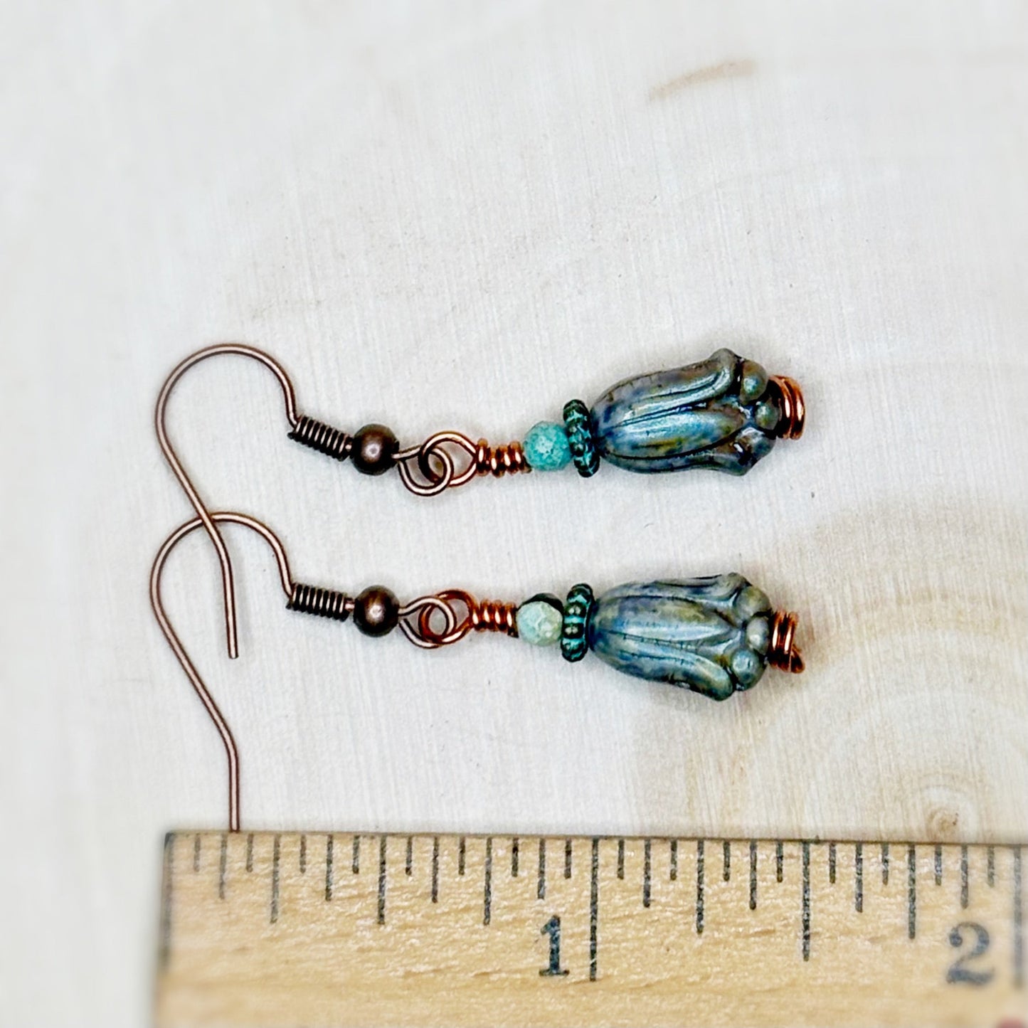Pair of beaded earrings with blue and green glass beads on a white background, shown next to a ruler for scale.