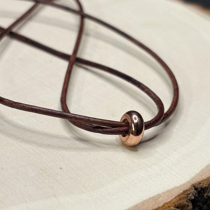 Close-up of a brown leather bracelet with a copper clasp on a light background