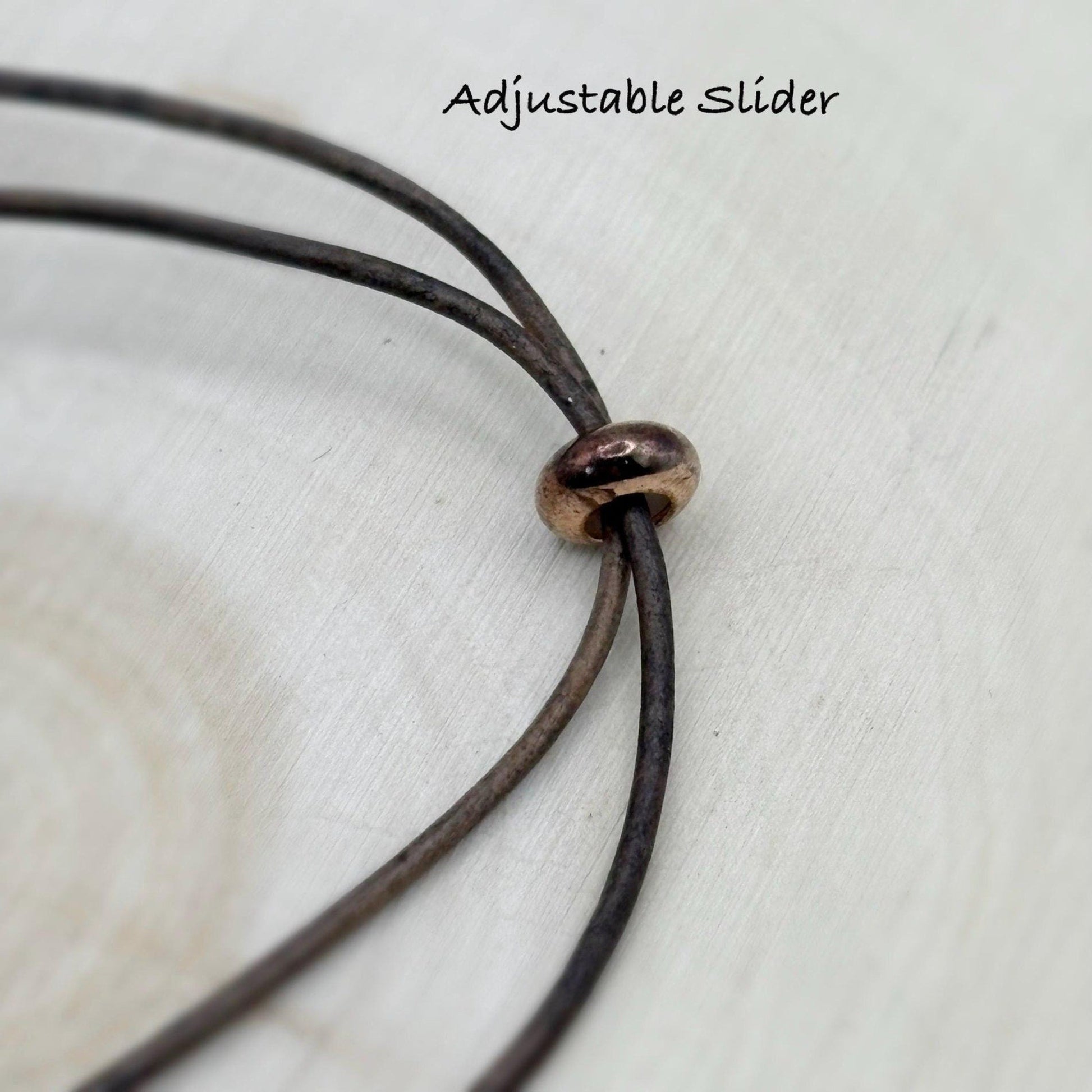 Close-up of a brown leather cord with an adjustable slider on a light wooden surface.