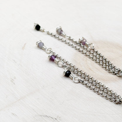 Silver chain necklace with purple and black beads on a light wooden surface