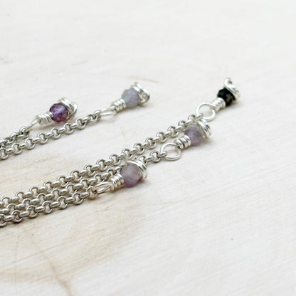 Silver chain necklace with purple gemstones on a light background