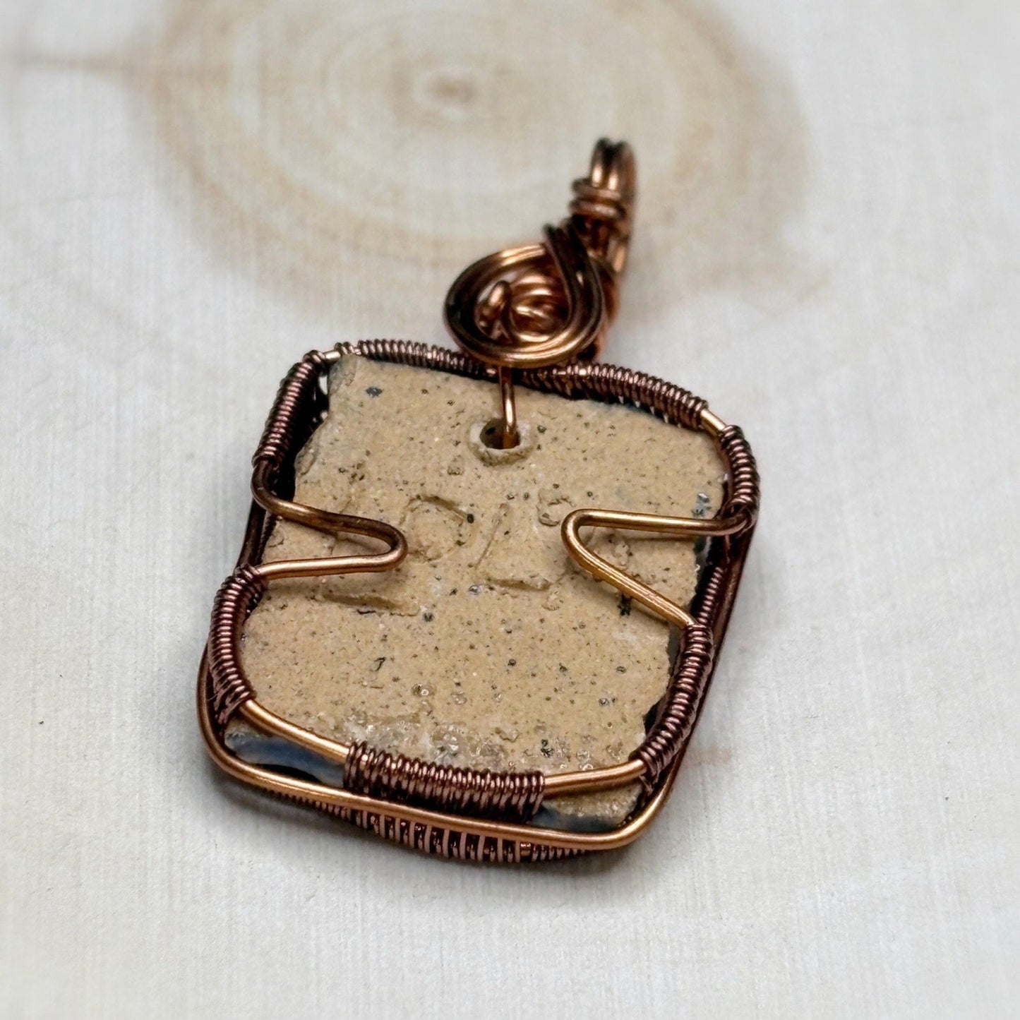 Copper-wrapped stone pendant on a white fabric background
