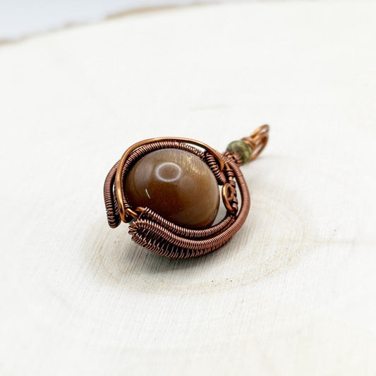 Copper-wrapped pendant with a brown stone on a white wood background