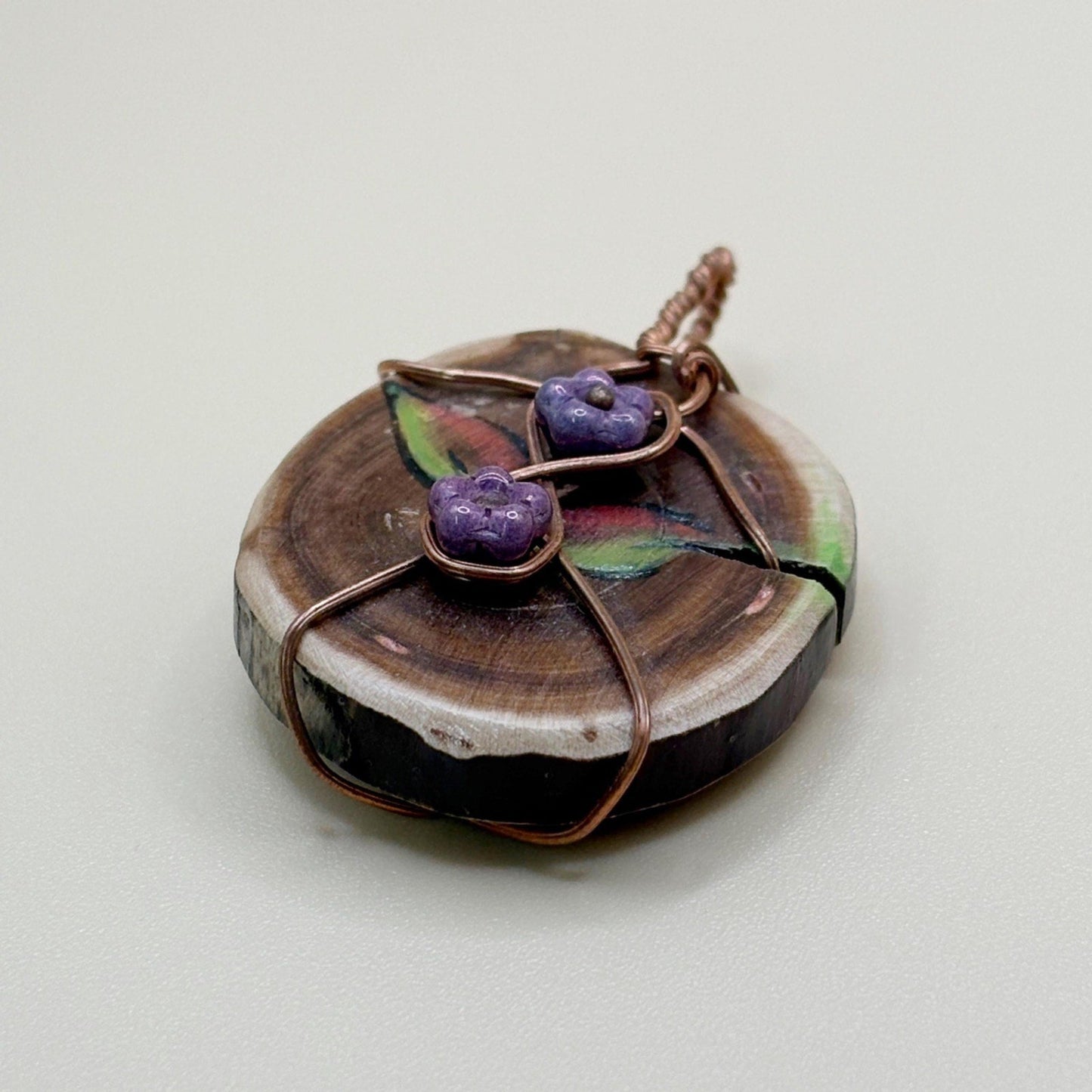 Handmade necklace with a wooden pendant and purple glass flowers on a light background
