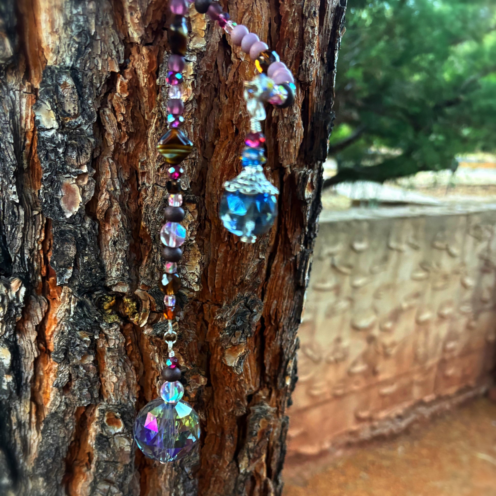 Colorful beaded sun catcher hanging on a tree trunk with a blurred background