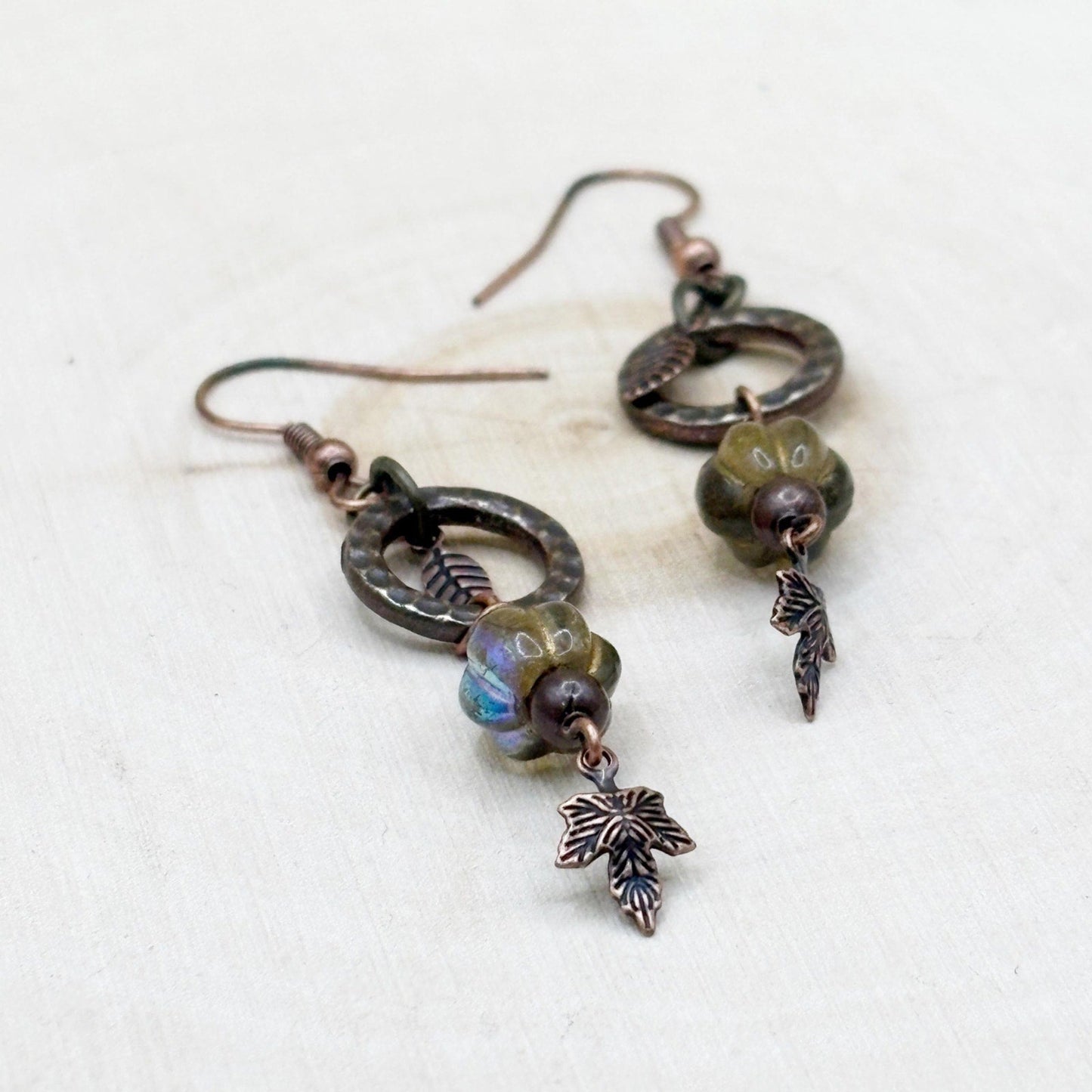 Pair of rustic copper earrings with leaf charms on a light background