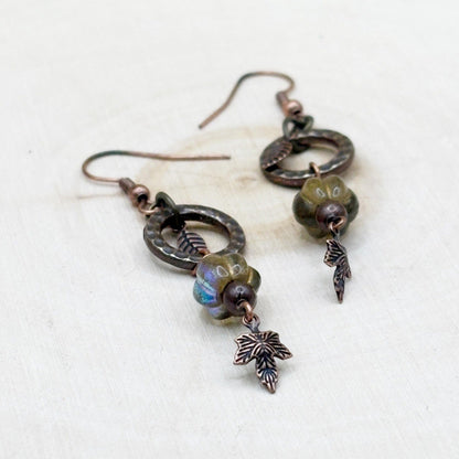 Pair of rustic copper earrings with leaf charms on a light background
