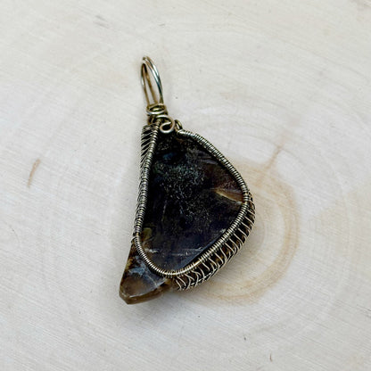 Teardrop-shaped pendant with wire wrapping on a light wooden background