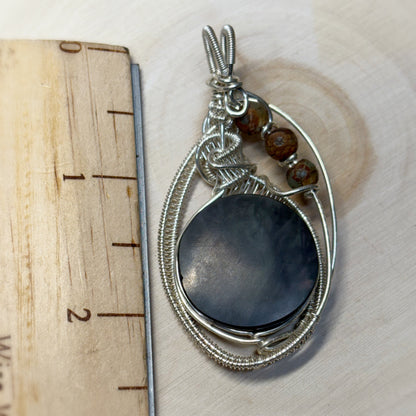 Silver pendant with a dark stone and beads on a wooden surface with a ruler for scale.