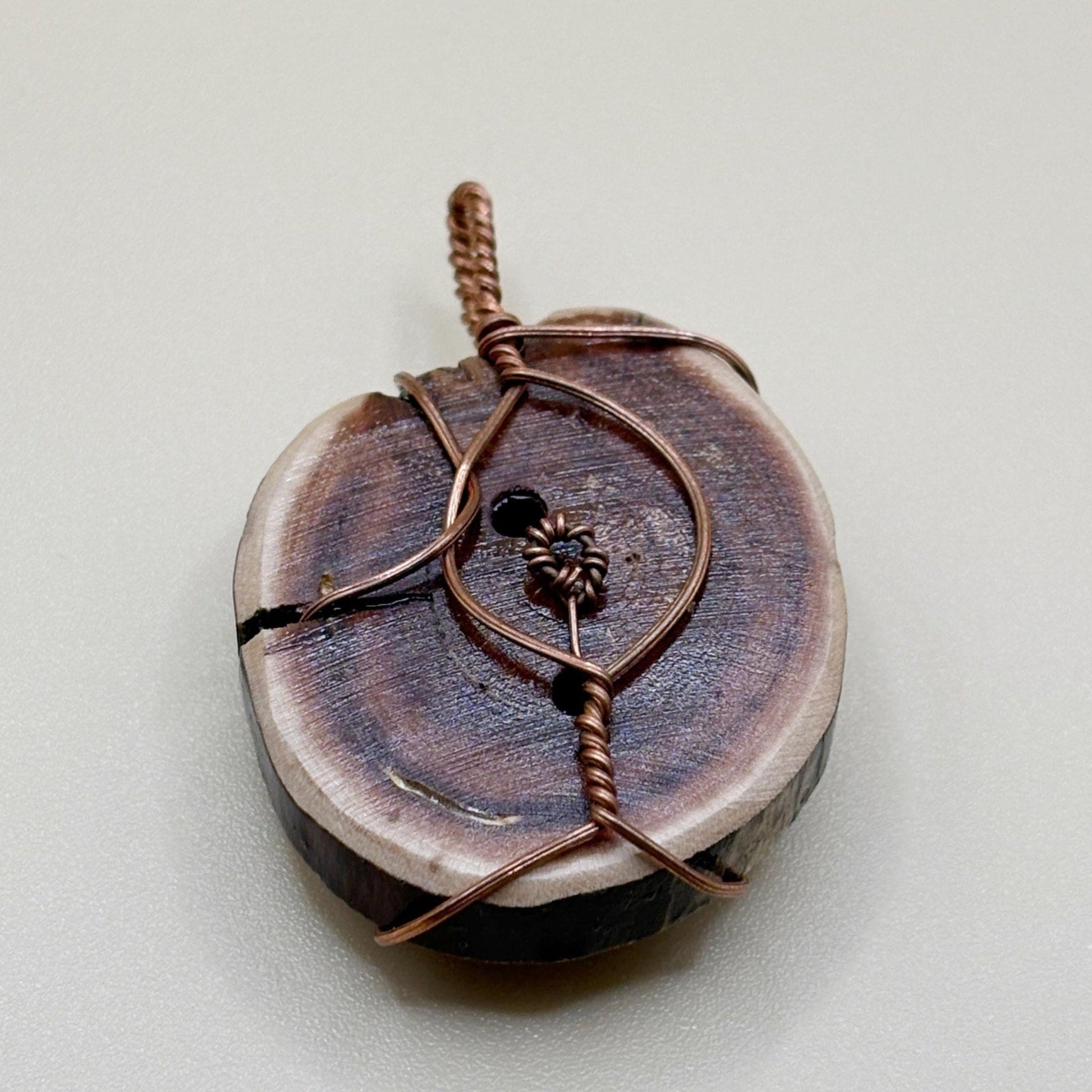 Wooden pendant with copper wire wrapping on a light gray background