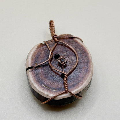Wooden pendant with copper wire wrapping on a light gray background