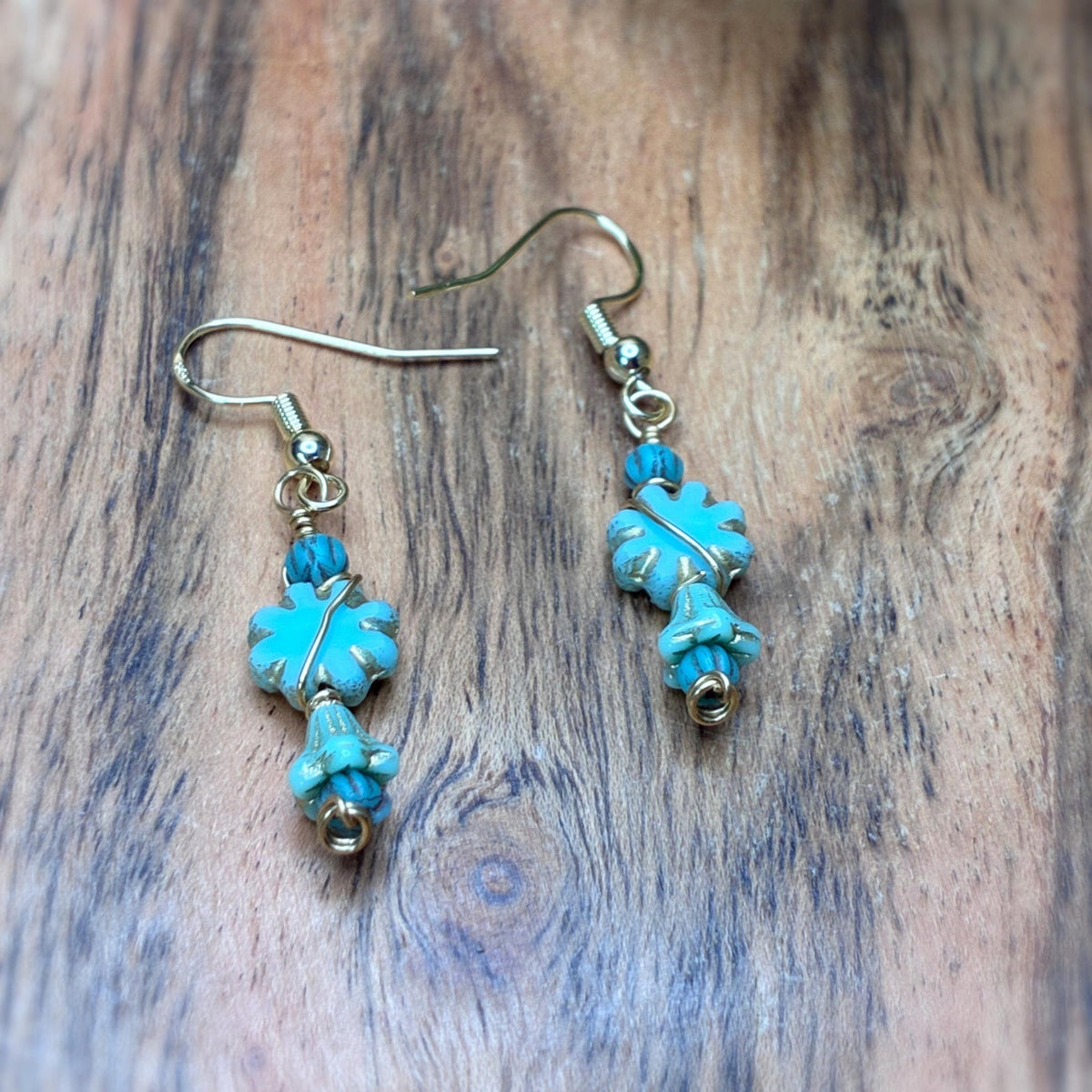 blue flower shaped earrings wire wrapped in gold tone wire laying on a wooden backround