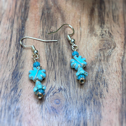 blue flower shaped earrings wire wrapped in gold tone wire laying on a wooden backround