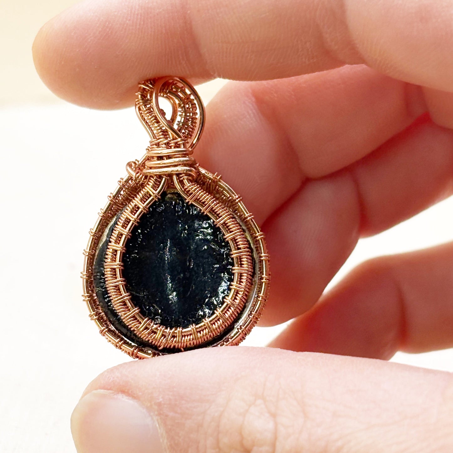 Hand holding a copper-wrapped pendant with a dark stone