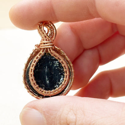 Hand holding a copper-wrapped pendant with a dark stone