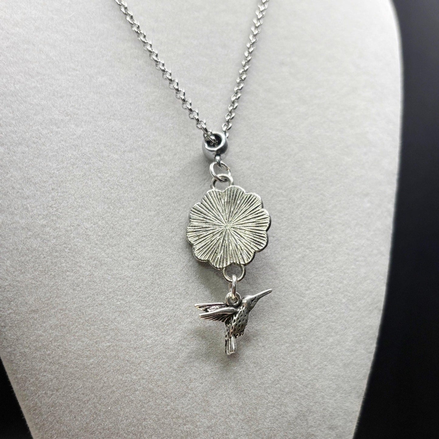 Silver necklace with a flower pendant and a small bird charm on a mannequin.