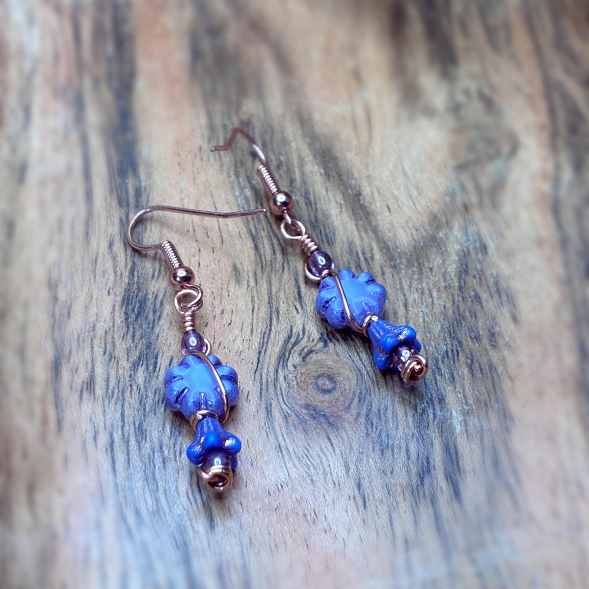 copper wire wrapped floral beaded earrings laying on a wooden background