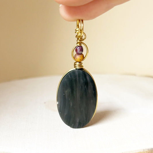 Necklace Pendant with a dark green stone and gold wire wrapping on a beige background