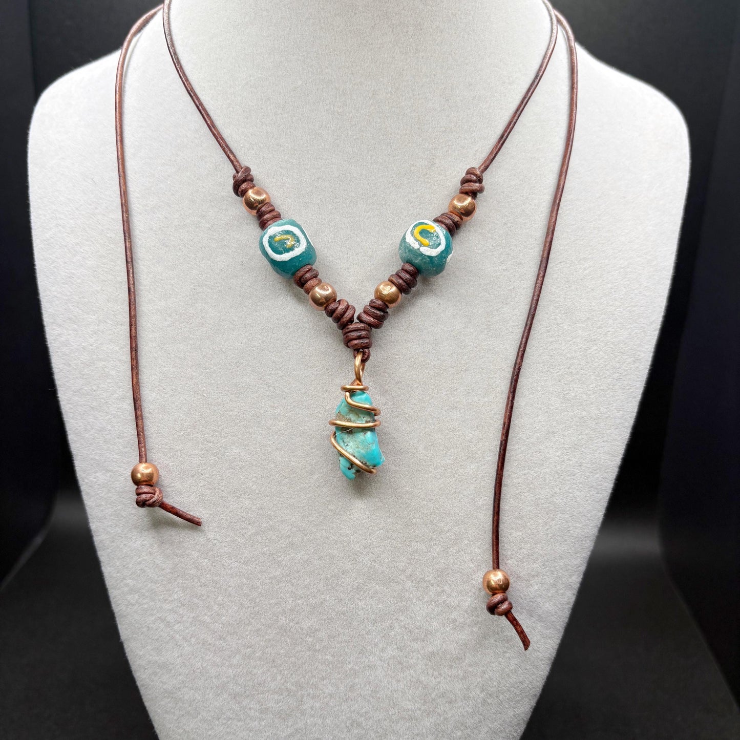 Necklace with turquoise beads and brown cord on a mannequin bust.