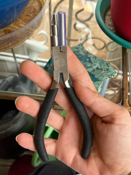 Hand holding a pair of pliers with black handles against a blurred background-p