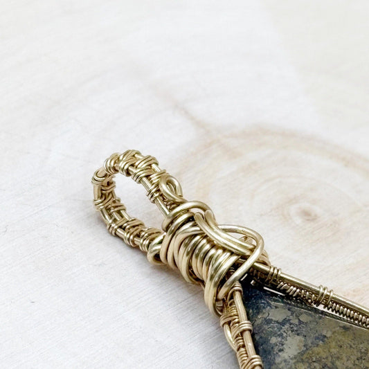 Decorative gold pyrite stone with intricate gold wire wrapping on a white wood background