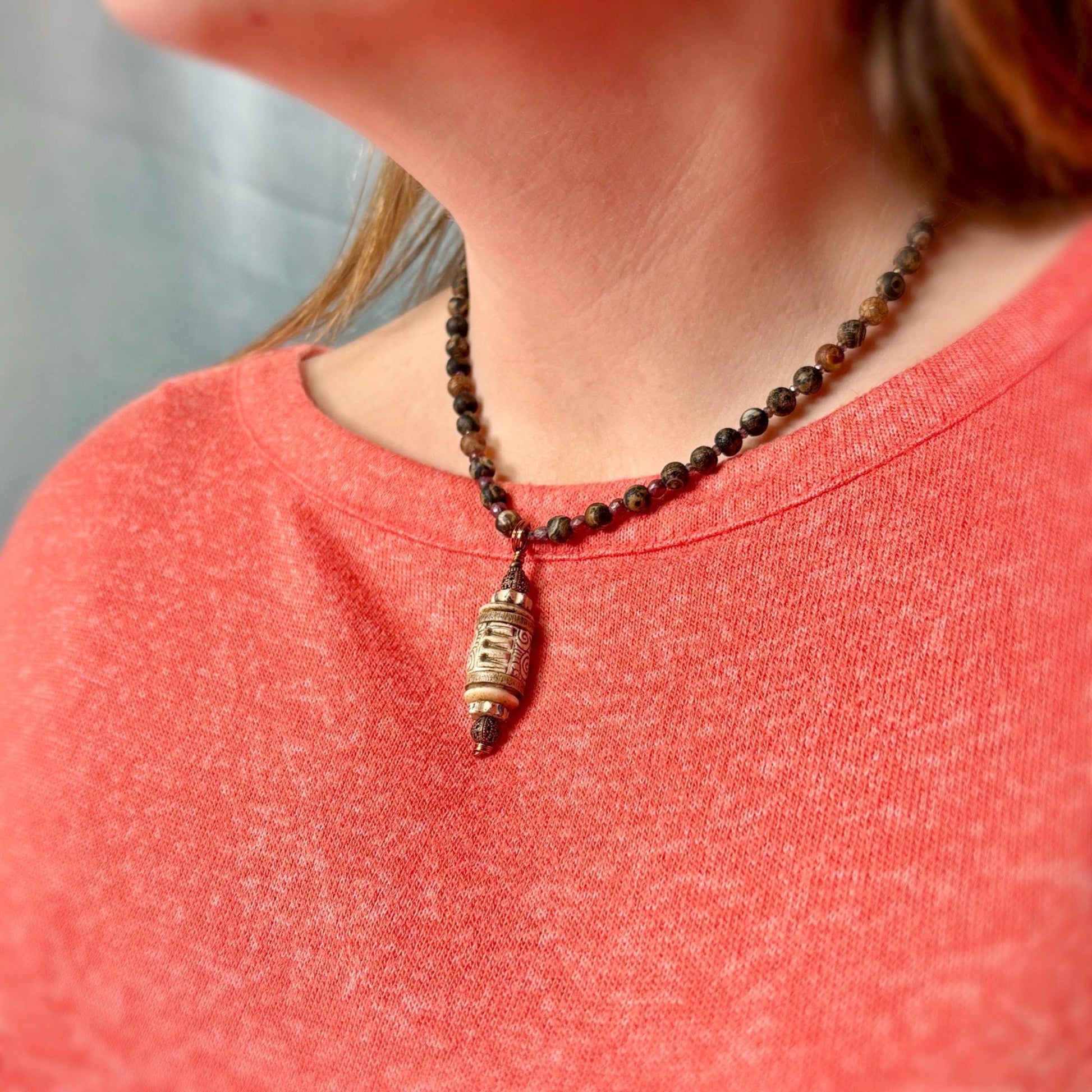 Person wearing a beaded necklace with a pendant on a red shirt