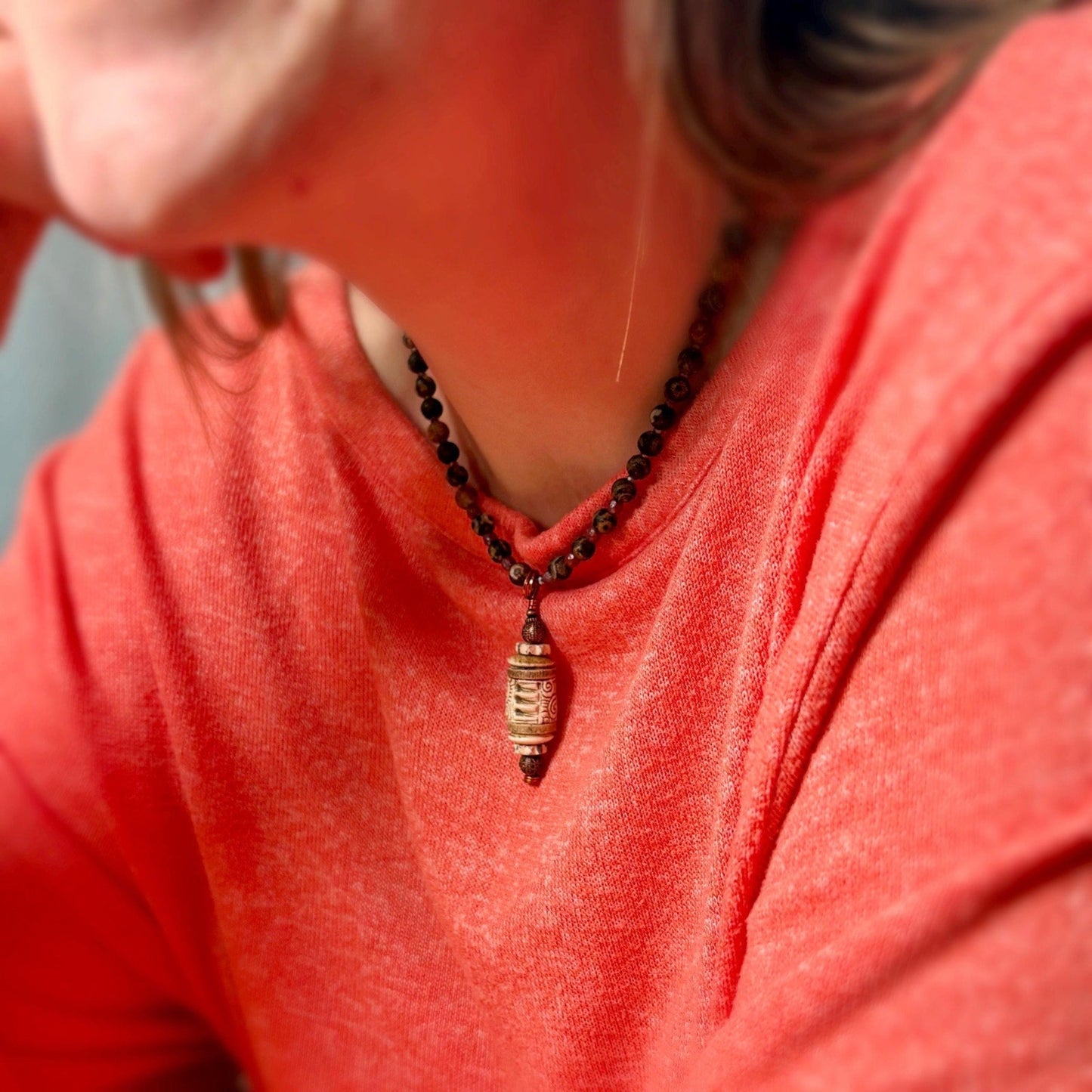 Person wearing a red shirt with a necklace featuring a large pendant.