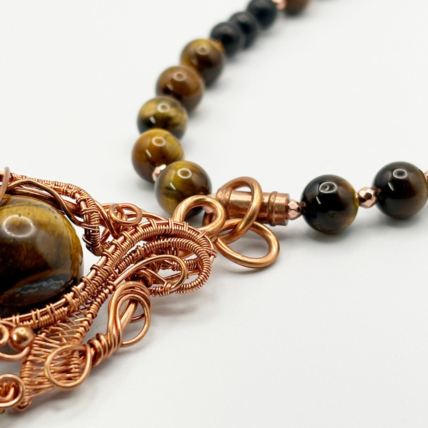Necklace with brown beads and intricate copper wirework on a white background
