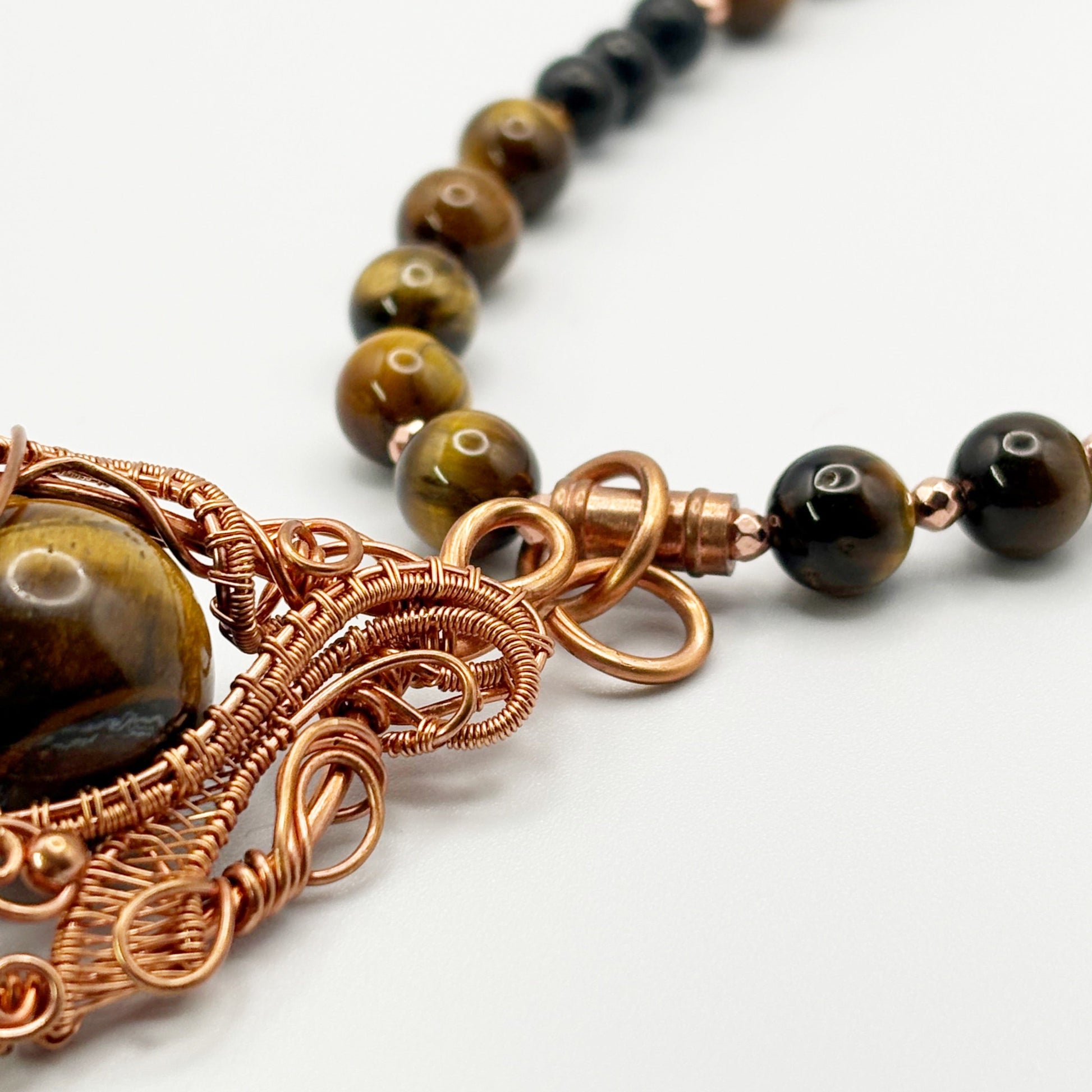 Necklace with brown beads and intricate copper wirework on a white background