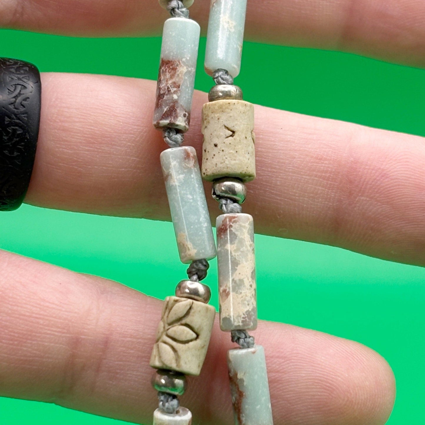 Close-up of a hand holding a beaded necklace with green background