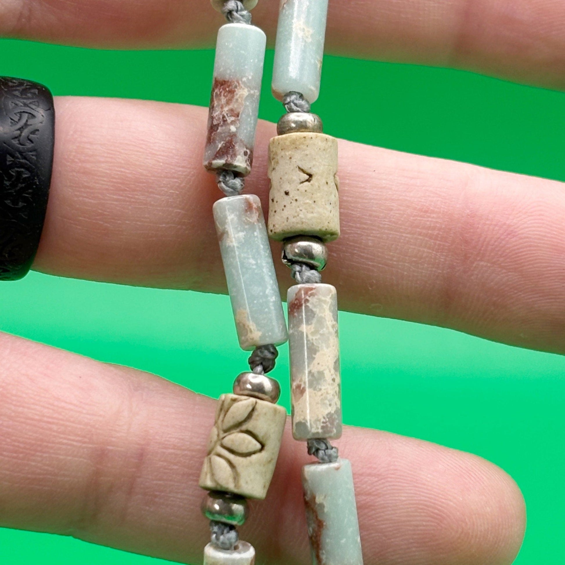 Close-up of a hand holding a beaded necklace with green background