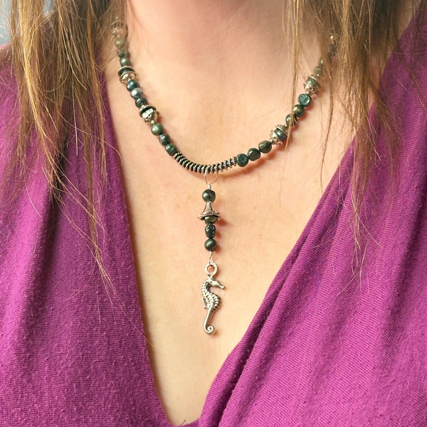 Necklace with green beads and a seahorse pendant worn by a person in a purple garment.