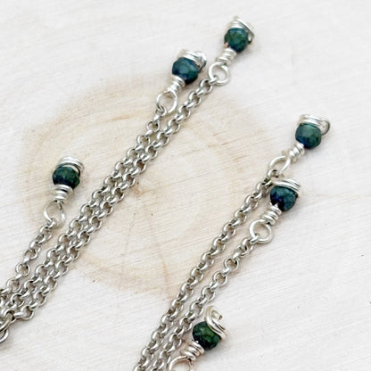 Silver chains with green beads on a light background