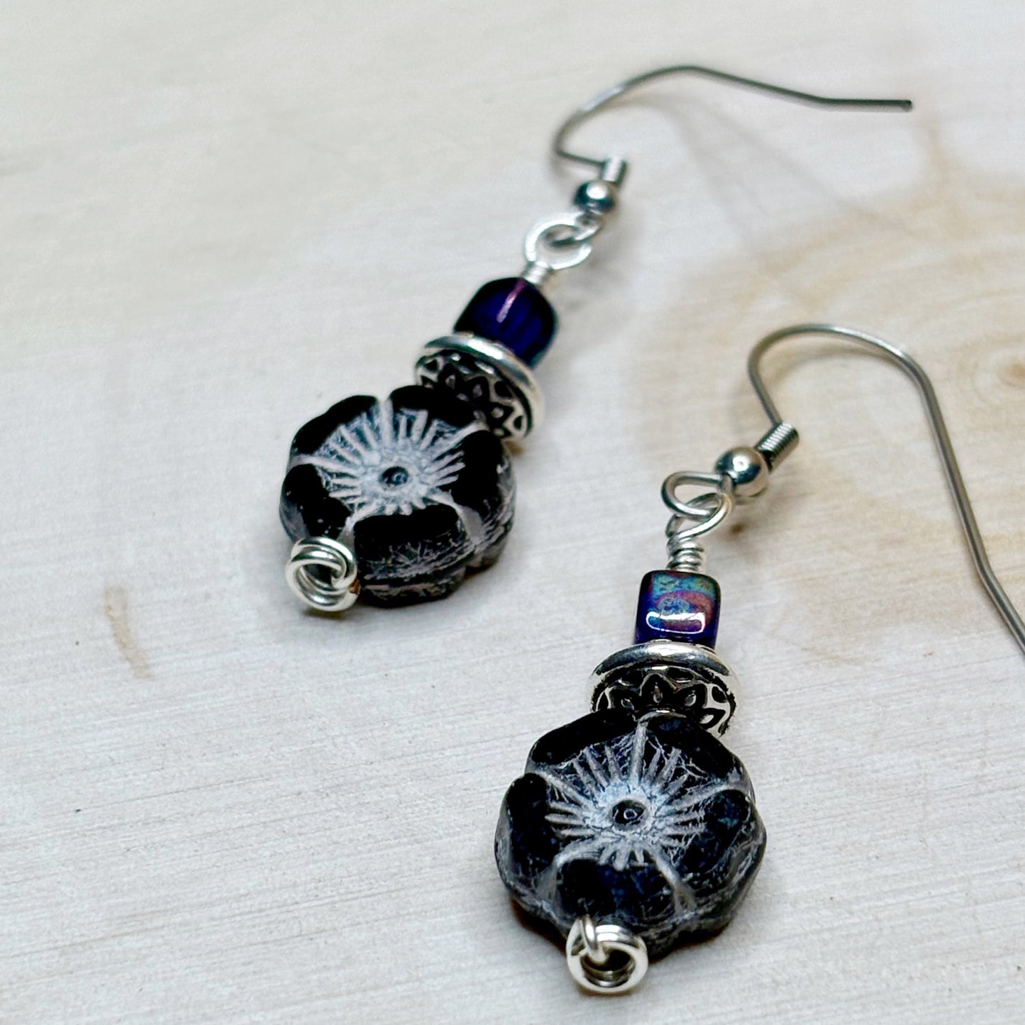 Pair of black floral-patterned earrings with silver and purple accents on a light background