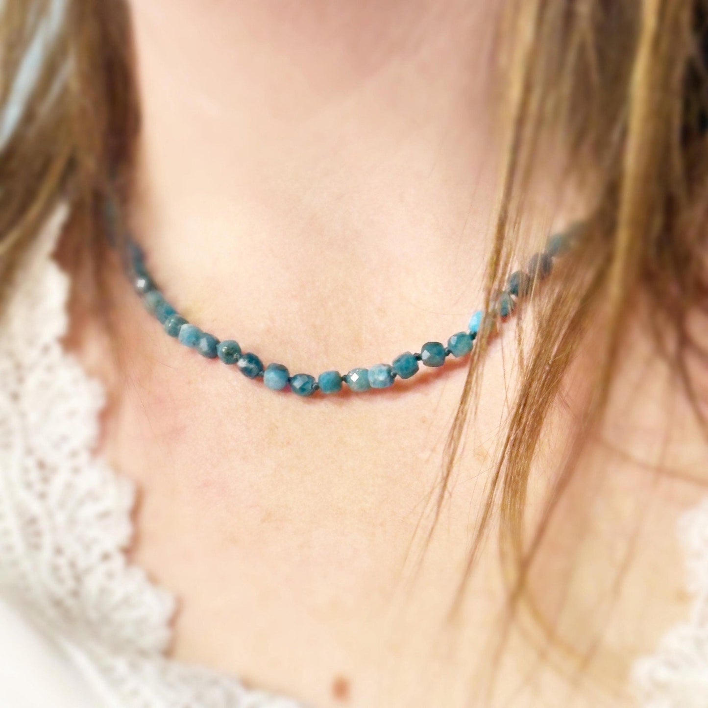 Close-up of a person wearing a blue beaded necklace with a blurred background