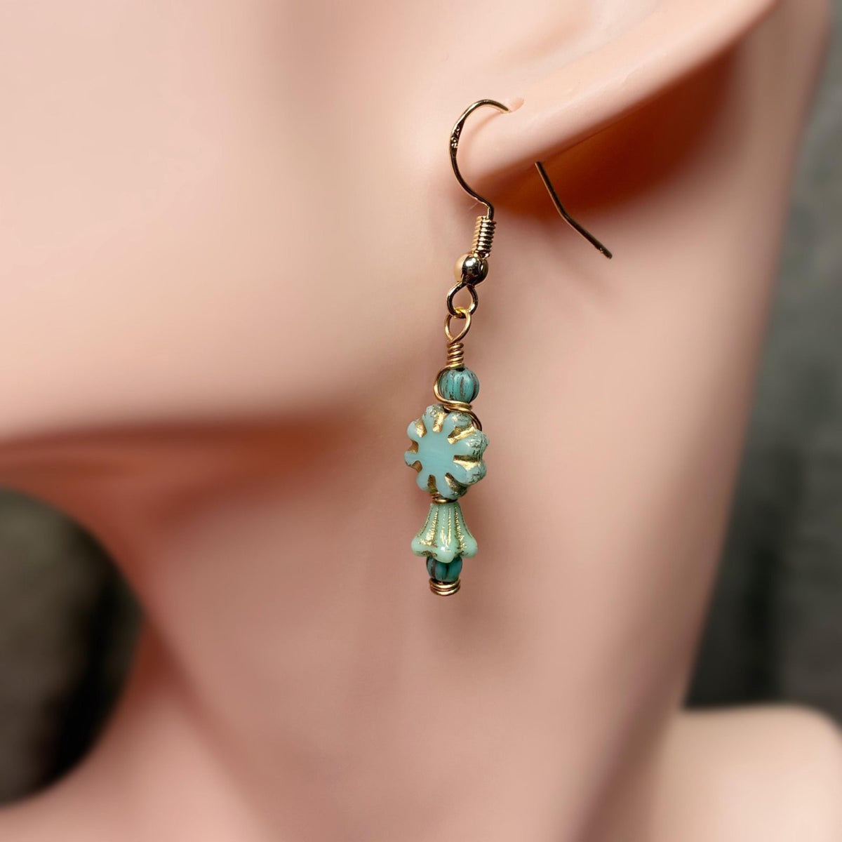 Gold tone earrings with blue beads that are floral shaped hanging on an ear lobe