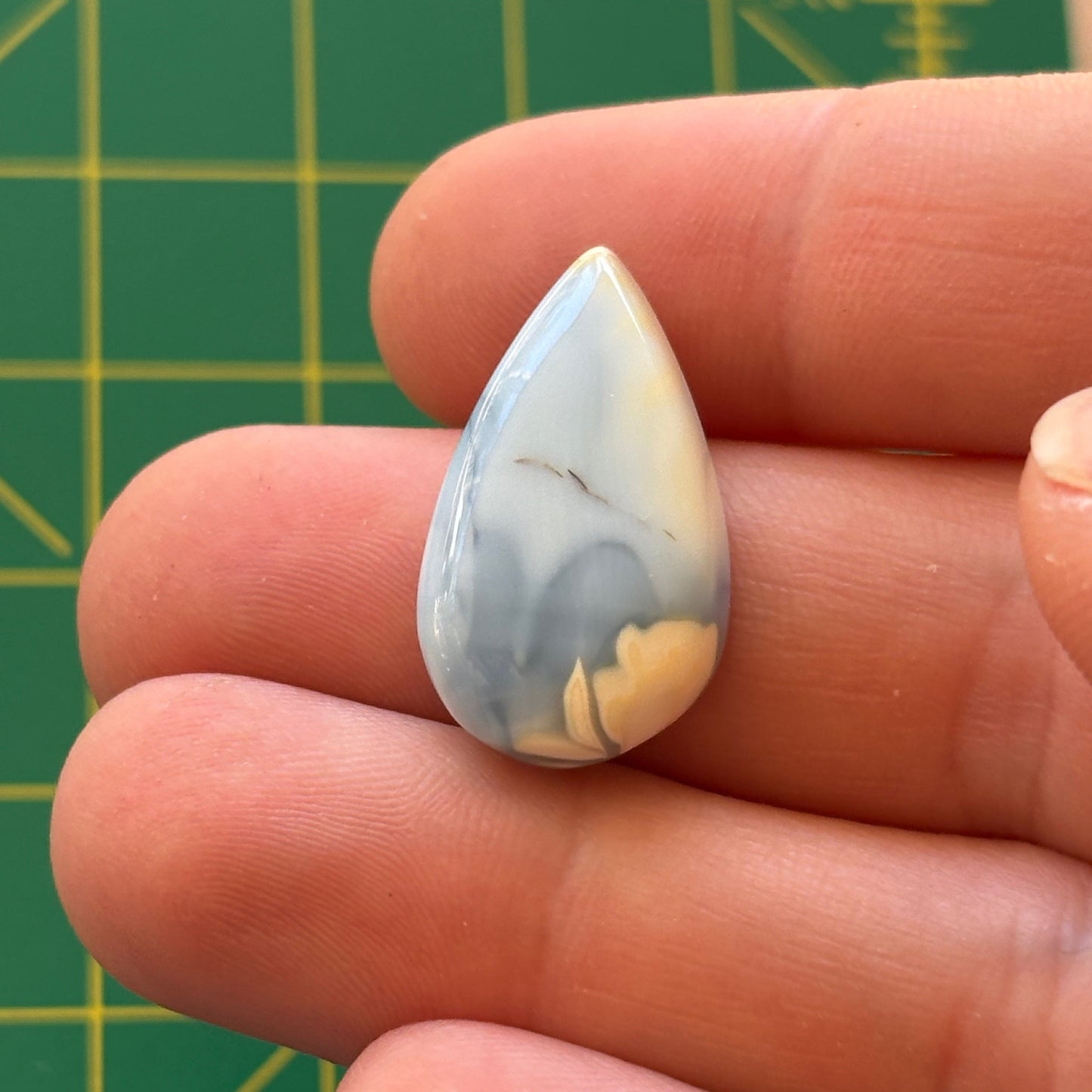 Teardrop-shaped stone held between fingers with a green grid background