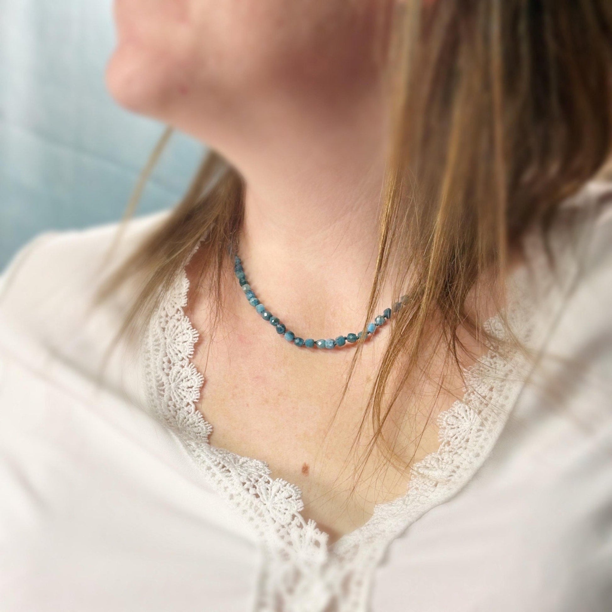 Person wearing a blue beaded necklace with a blurred background